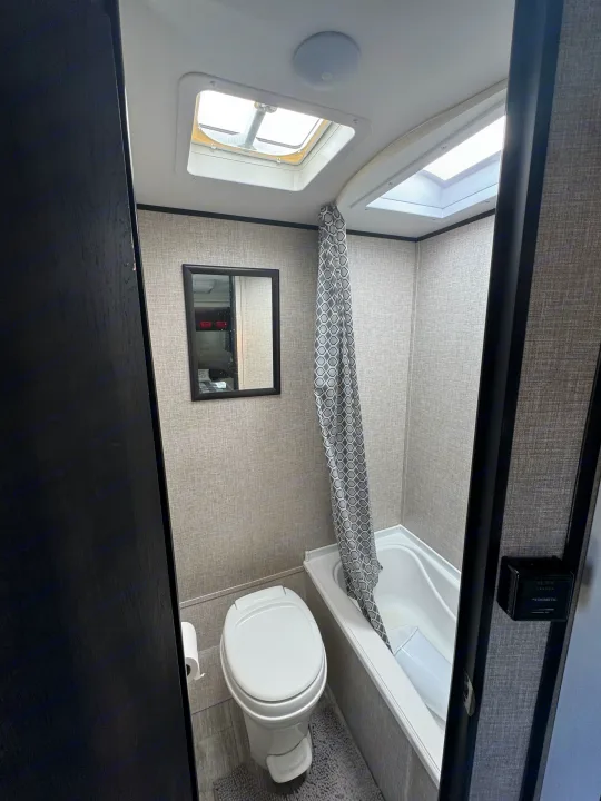 A compact RV rental bathroom featuring a toilet, bathtub/shower combo with curtain, and natural light from skylights.. Jayco Jay Flight SLX 2022