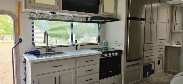 Modern RV rental kitchen with sleek appliances, ample storage, and a bright window.. Mercedes Coleman 24CL 2024