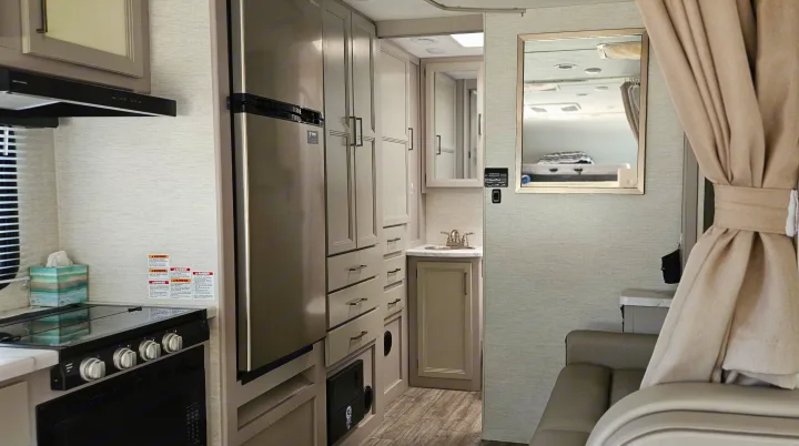 Compact RV rental interior featuring a modern kitchen, vanity sink, lounge seating, and bedroom area reflected in the mirror.. Mercedes Coleman 24CL 2024