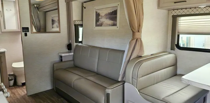 Spacious RV rental interior with a light-colored couch, dinette, and discreet bathroom area, showcasing compact modern living.. Mercedes Coleman 24CL 2024