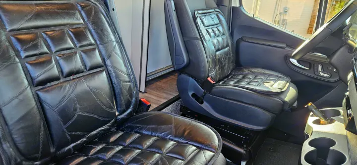 Comfortable RV rental interior showing black quilted seat covers on both driver and passenger seats, with a bright cabin.. Mercedes Coleman 24CL 2024