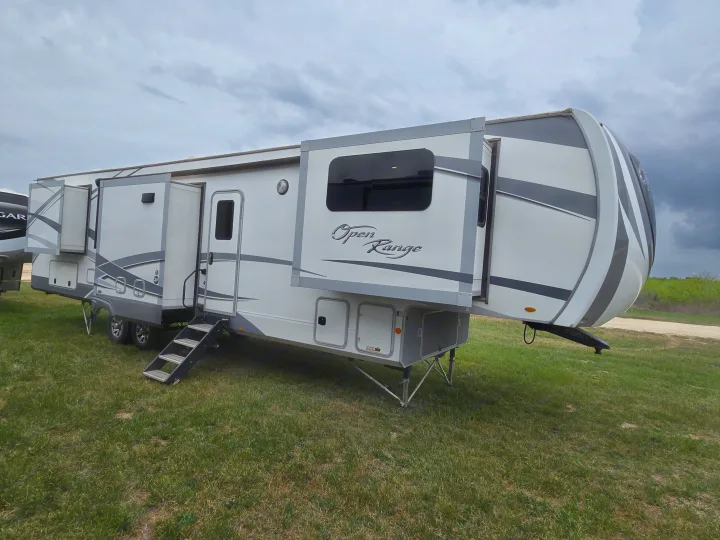 Spacious Open Range fifth-wheel RV rental, white and gray with extended slide-outs, parked on green grass.. Open Range Highland Ridge 2021