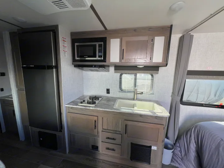 Compact RV rental kitchen features fridge, microwave, stovetop, and sink, optimizing space in this modern travel trailer.. Gulf Stream Kingsport 2021