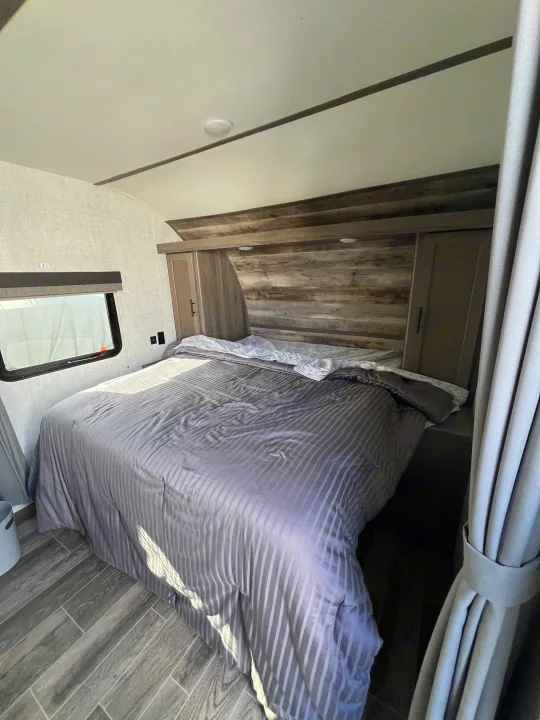 This RV rental bedroom features a comfy bed with striped bedding, wood-look headboard, storage, and an exit window.. Gulf Stream Kingsport 2021