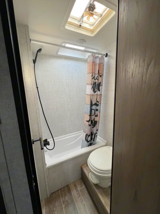 RV rental's compact bathroom with shower/tub combo, toilet, and ceiling fan via skylight.. Gulf Stream Kingsport 2021