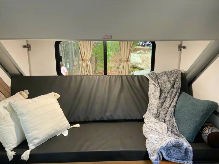 Cozy RV rental interior: black couch with white/teal pillows & gray blanket, offering a scenic campsite view.. A-Liner Ranger 2025