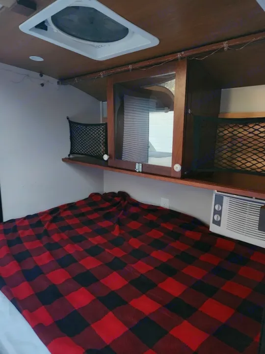 RV rental interior: Plaid bed, overhead storage, AC unit, and ceiling fan.. Driftwood Custom 2021