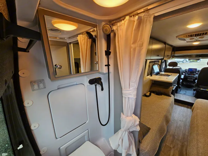 Inside an RV rental: a compact camper van bathroom with shower, mirror, and toilet, adjacent to the living/kitchen area.. Thor Motor Coach Twist 2026