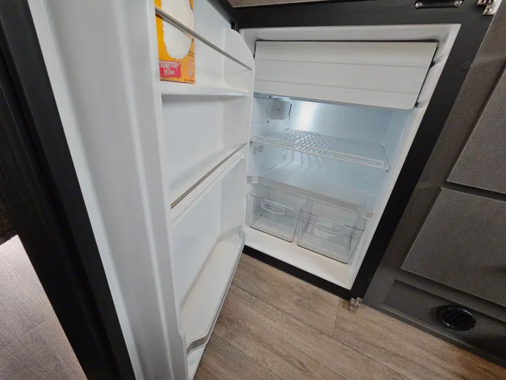 A clean, open refrigerator in an RV rental, showcasing wire shelves and clear storage bins, ready for your trip's provisions.. Thor Motor Coach Twist 2026