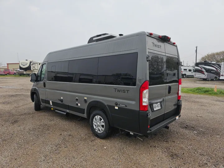 Gray Twist camper van on gravel, equipped with solar and side hookups, ready for rv rental. Other recreational vehicles in background.. Thor Motor Coach Twist 2026