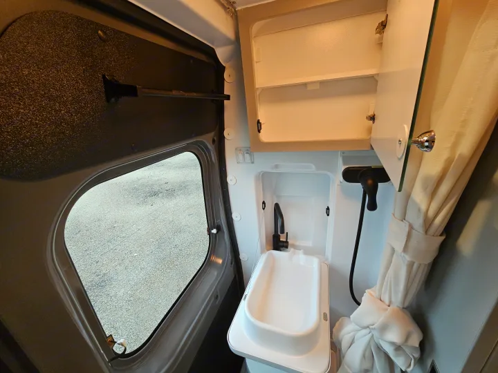 Inside an RV rental: a compact wet bath with sink, faucet, shower, storage cabinet, and window providing natural light.. Thor Motor Coach Twist 2026