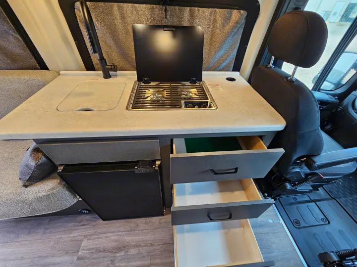 Inside an RV rental, showcasing a compact kitchen with Dometic stovetop, sink, Nova Kool fridge, and pull-out drawers.. Thor Motor Coach Twist 2026