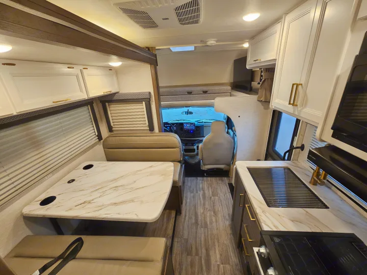 Modern RV rental interior: kitchen with sink/stove, dinette, and bright cockpit view. Ideal for your next trip.. Thor Motor Coach Four Winds 2026