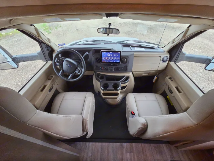 Step inside this modern RV rental: a spacious front cabin with tan seats, a Ford dashboard, and infotainment system.. Thor Motor Coach Four Winds 2026