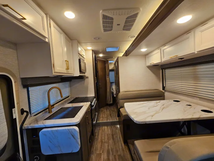 Step inside this modern **RV rental**! Features a full kitchen with gold hardware, dining booth, and ample living space.. Thor Motor Coach Four Winds 2026