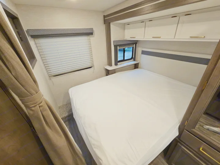 Clean RV rental bedroom with a white bed, overhead cabinets, and windows including one with an "EXIT" sign.. Thor Motor Coach Four Winds 2026