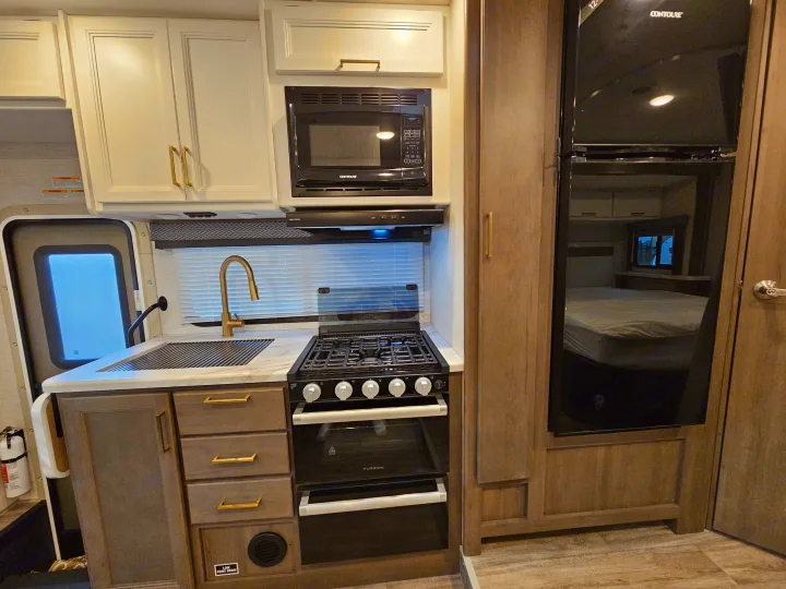 Step inside this modern RV rental kitchen. Features include a sink, microwave, gas range, refrigerator, and ample storage.. Thor Motor Coach Four Winds 2026