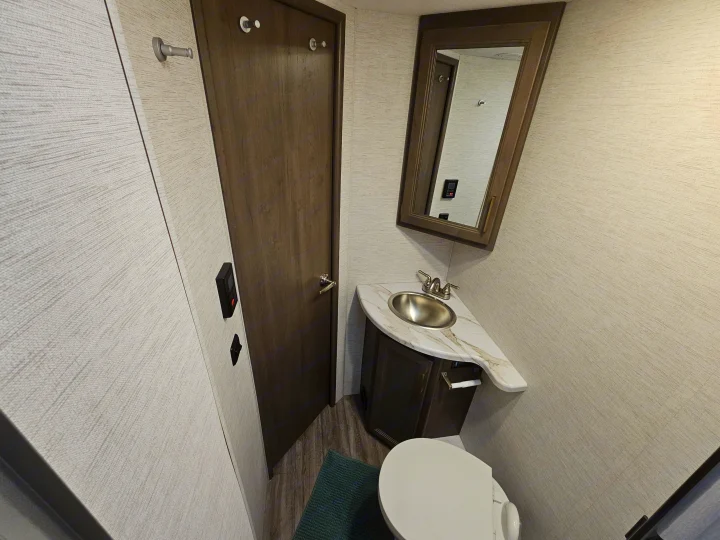 Step inside this modern RV rental's compact bathroom. Features include a toilet, sink with vanity, mirror, and textured walls.. Thor Motor Coach Four Winds 2026
