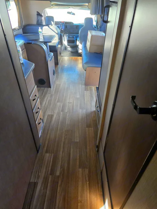 Clean rv rental interior with wood-look flooring, a dinette on the left, and the front cab visible in a well-lit living space.. Thor Majestic 2019