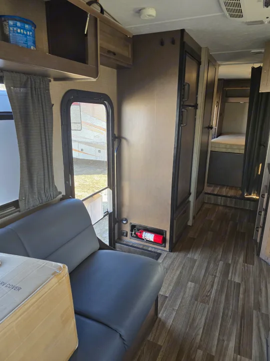 RV rental interior: sofa, open entry door showing outside, mounted fire extinguisher, refrigerator, and bedroom down the hall.. Thor Majestic 2019