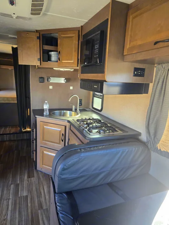 RV rental interior: kitchen with stove, sink, microwave, cabinets, and dining bench. Bunk beds visible.. Thor Majestic 2019