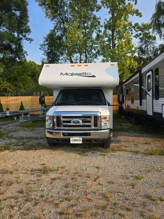 A white Majestic Class C RV rental (Ford motorhome) is parked on a gravel lot, showing its front and a Cruise America plate.. Thor Majestic 2019