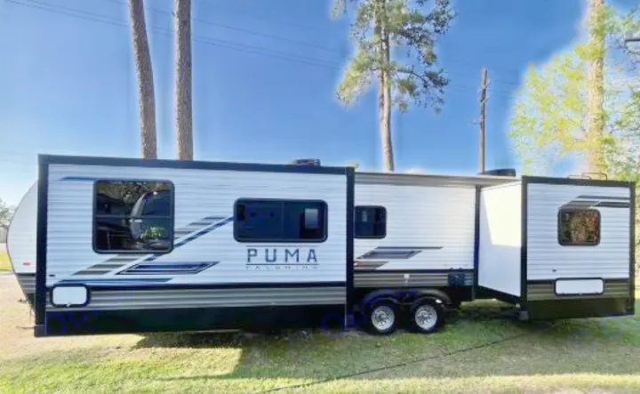 White Puma Palomino travel trailer with extended slide-outs, ready for an RV rental. Parked outdoors on grass.. Forest River Palomino Puma 2021