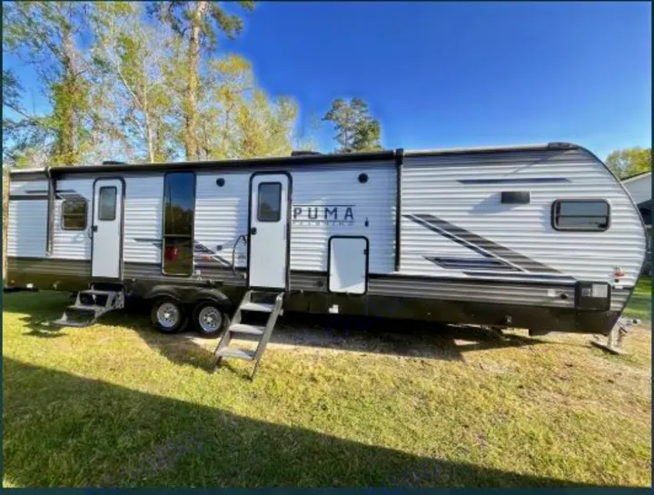 A modern grey Puma travel trailer RV, parked on grass with steps extended. An ideal rv rental for outdoor getaways.. Forest River Palomino Puma 2021