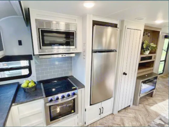 Explore this modern RV rental's full kitchen with stainless steel microwave, oven range, and fridge, plus storage cabinets.. Forest River Palomino Puma 2021