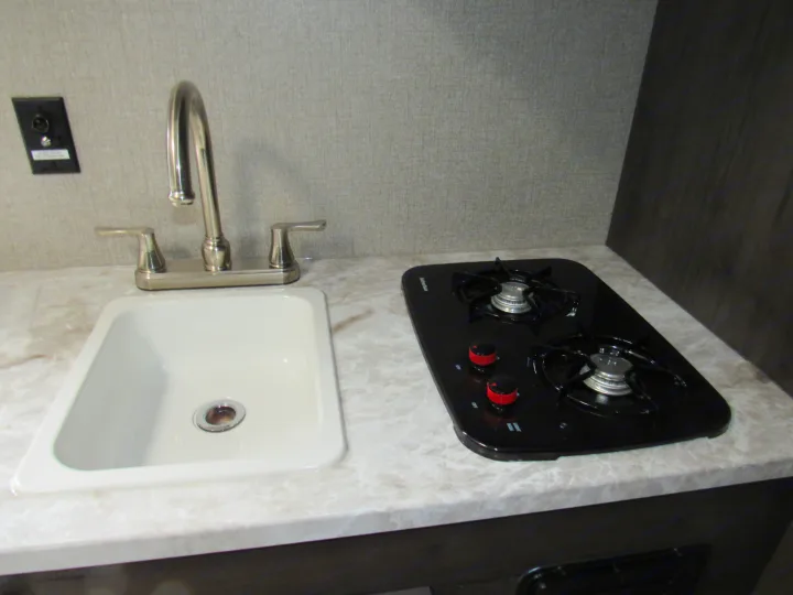 Compact RV rental kitchen with white sink, chrome faucet, black two-burner stovetop, and patterned counter.. Jayco Jay Flight SLX 2021