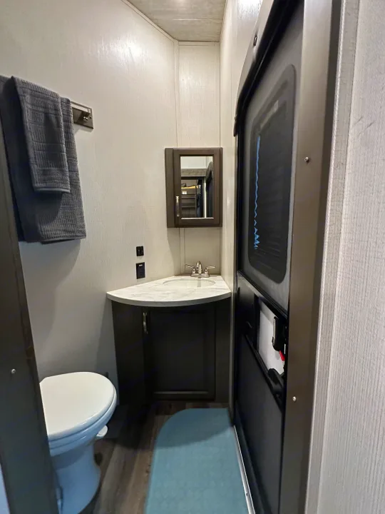 Compact RV rental bathroom features a toilet, corner sink, mirror, and a towel rack with gray towels.. Keystone RV Cougar 2021