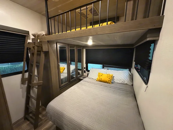 RV rental bedroom view: main bed with yellow pillow, a ladder leading to a cozy overhead loft bunk, and mirrored storage.. Keystone RV Cougar 2021