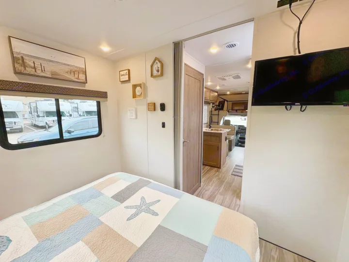 This inviting rv rental features a cozy bedroom with a starfish quilt, TV, and open living space.. Gulf Stream Conquest 2025