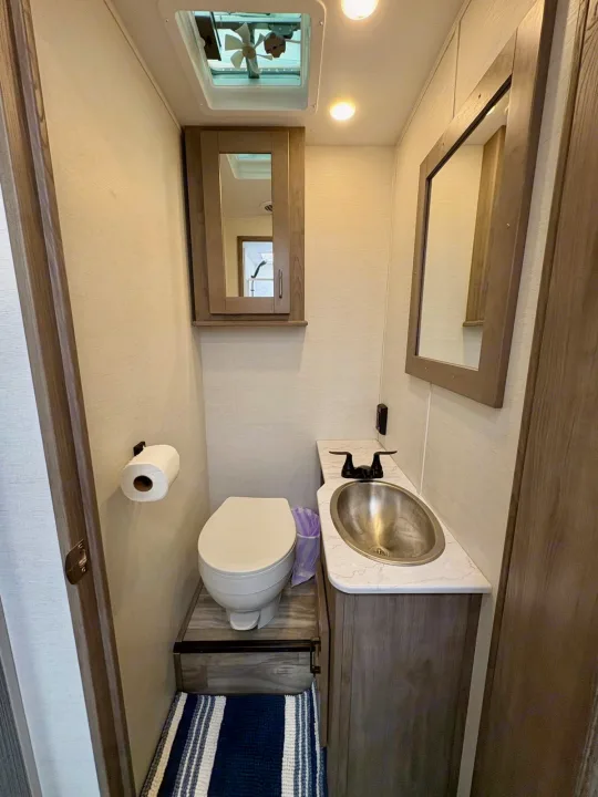 Inside a functional RV rental bathroom: toilet on a raised base, vanity with sink, mirrored cabinet, and vent fan.. Gulf Stream Conquest 2025