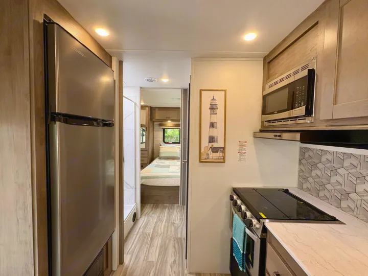 Spacious RV rental interior featuring a modern kitchen with stainless steel fridge, microwave, stovetop, and a cozy bedroom.. Gulf Stream Conquest 2025