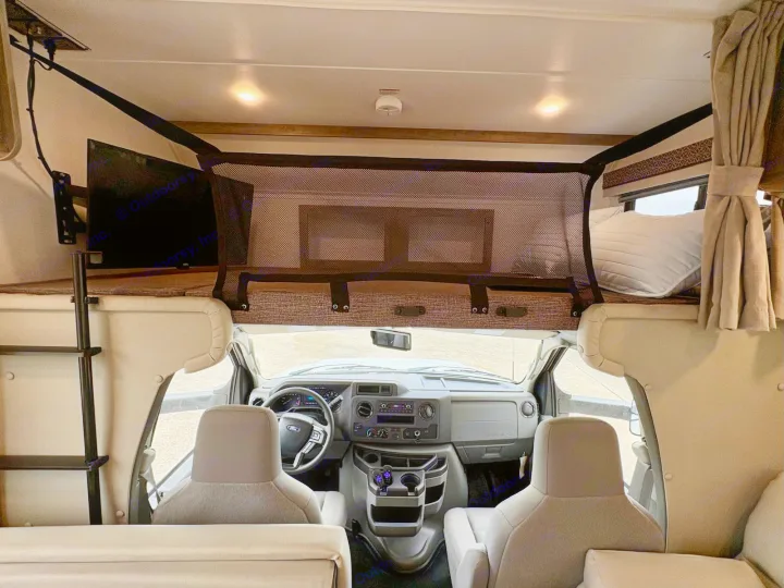 RV rental interior: cockpit, front seats, and overhead bunk bed with safety net and TV. Ready for adventure!. Gulf Stream Conquest 2025