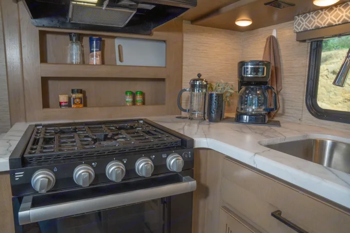 Well-appointed rv rental kitchen showing gas range, coffee maker, sink, and open shelving for cooking ease.. Thor Motor Coach Coleman 2023