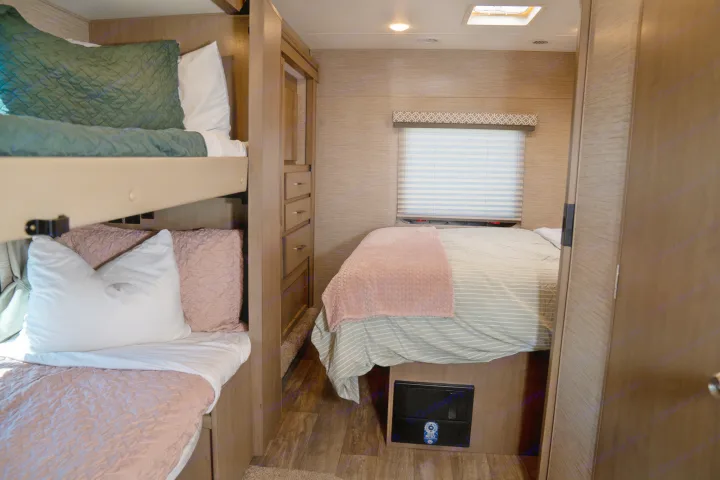 Cozy RV rental bedroom featuring comfortable bunk beds (green and pink) on the left and a striped main bed on the right.. Thor Motor Coach Coleman 2023