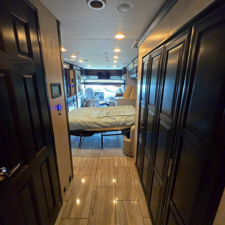 Explore a comfortable RV rental interior: a long hallway leads past dark wood cabinetry to a bed and the front cockpit. Modern flooring.. Berkshire XL 2022