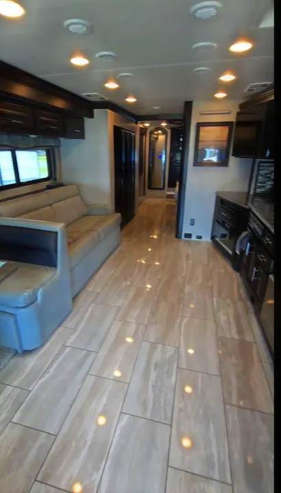 Modern rv rental interior with light-colored tile flooring reflecting ceiling lights, a beige sofa, and dark wood accents.. Berkshire XL 2022
