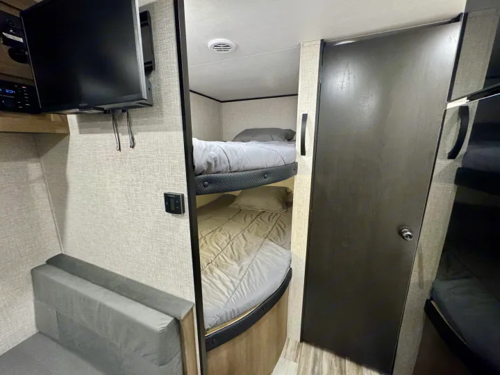 RV rental interior features bunk beds, a gray sofa, and TV for a compact, functional living area.. Jayco 260BH 2025