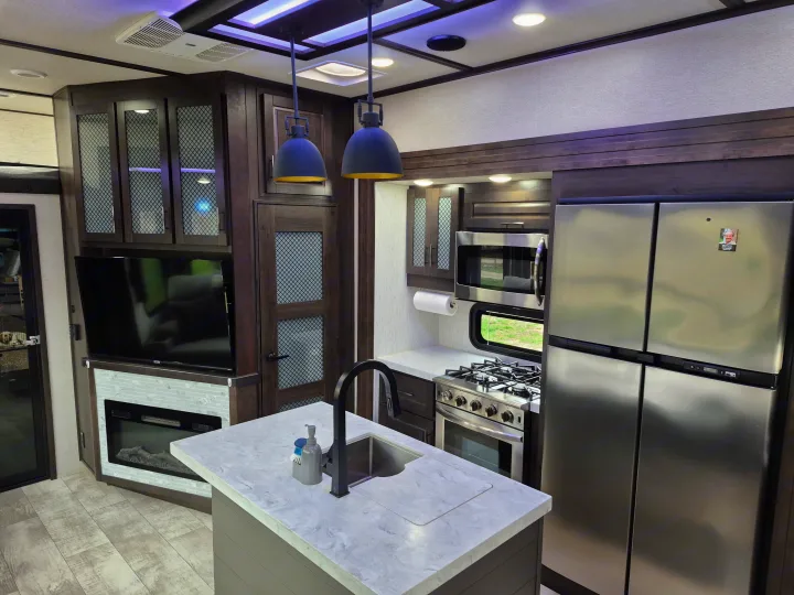 Spacious RV rental showcasing a modern kitchen with island, stainless steel appliances, plus a living area with TV & fireplace.. Grand Design Momentum 2022