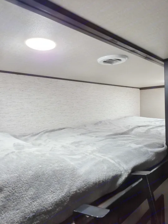 Inside an RV rental: A cozy bunk bed with a soft gray blanket, ceiling light, and air vent visible.. Grand Design Momentum 2022