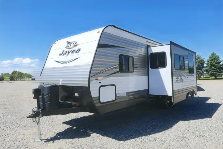 A white and gray Jayco travel trailer (RV) with an extended side, parked on gravel. An ideal rv rental for outdoor trips.. Jayco Jay Flight 2017