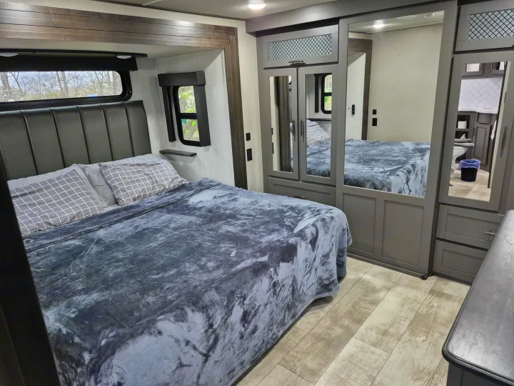 Spacious RV rental bedroom with a comfortable bed, mirrored closet, and a glimpse into the connected bathroom.. Grand Design Momentum 2022