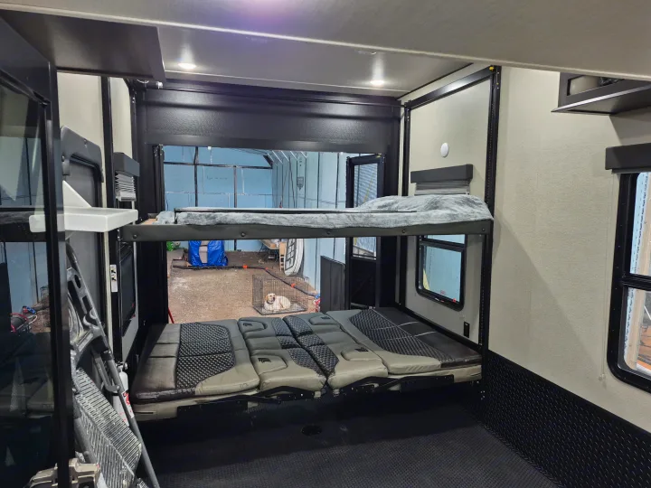 RV rental garage interior with convertible bunk beds and seating. A dog in a crate is visible through the open rear ramp.. Grand Design Momentum 2022