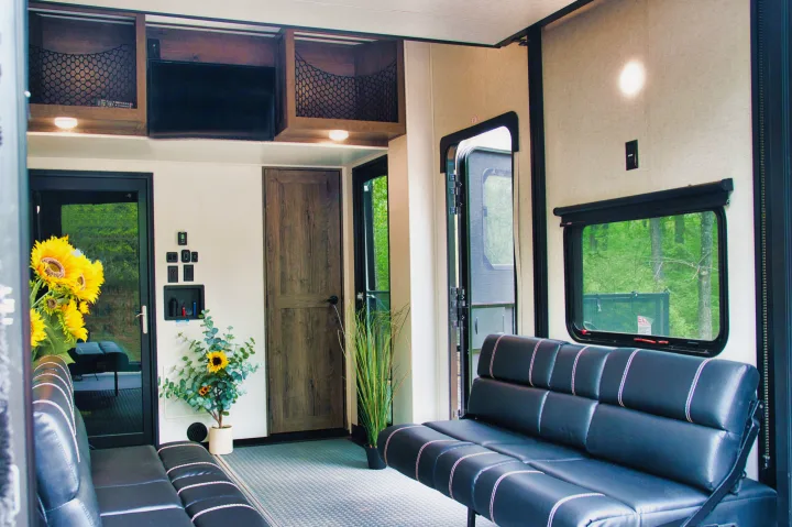 Comfortable RV rental interior. Features black benches with white stitching, TV, and wooded views through doors & windows.. Alliance Valor 2022