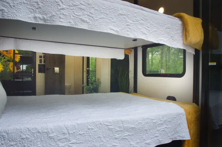 An RV rental's interior with comfy bunk beds, quilted white bedding, and green outdoor views for a relaxing stay.. Alliance Valor 2022
