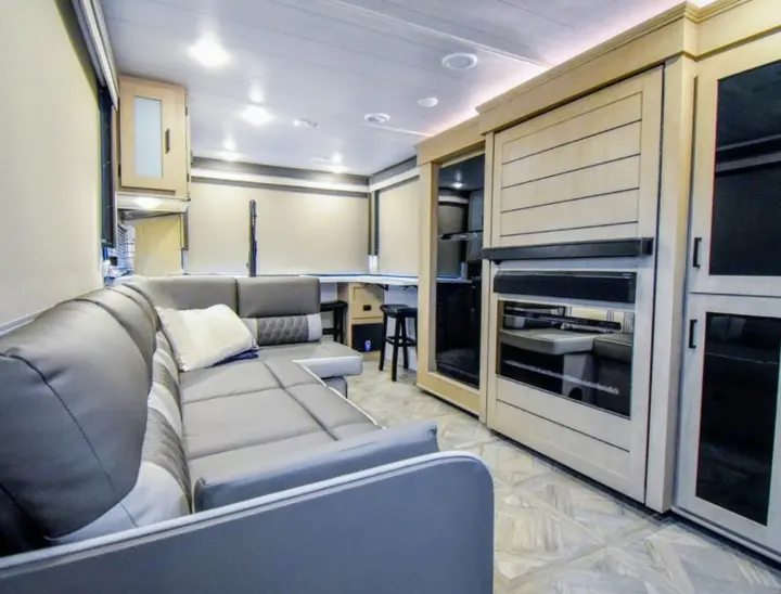 Spacious modern RV rental interior featuring a gray L-shaped sofa, entertainment center, and desk with stools.. Forest River Salem Cruise Lite 2024