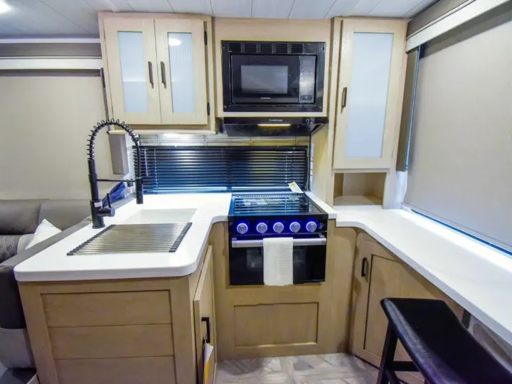 Modern rv rental kitchen with a black faucet, white countertops, stove, microwave, and light wood cabinets.. Forest River Salem Cruise Lite 2024